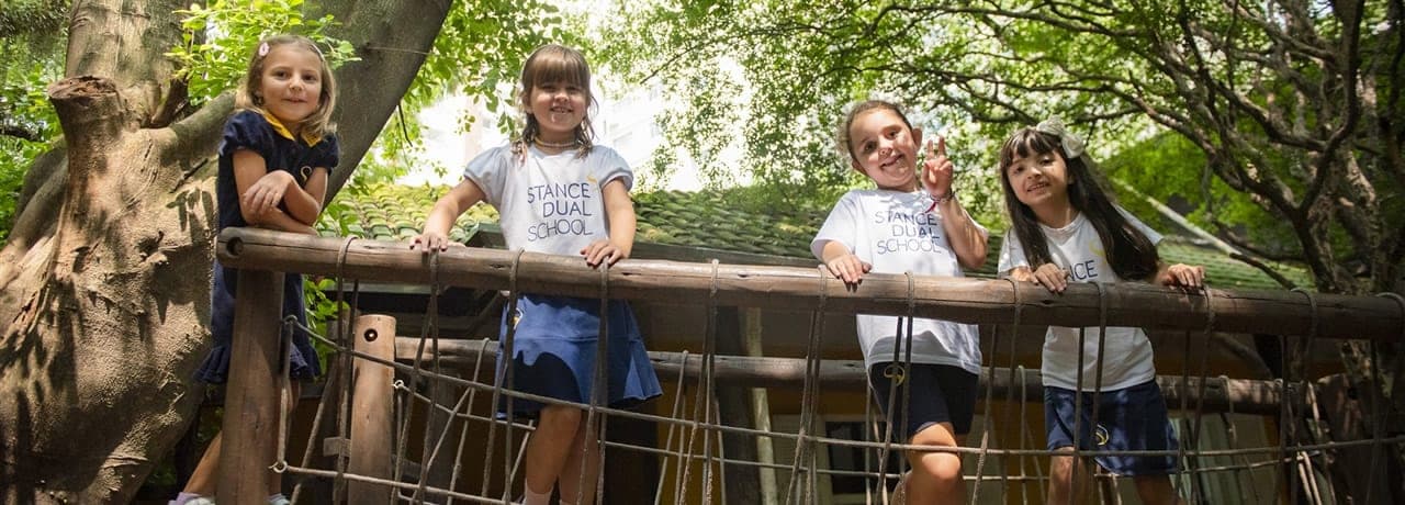 Quatro alunas sorridentes com uniforme da escola em uma casa na árvore