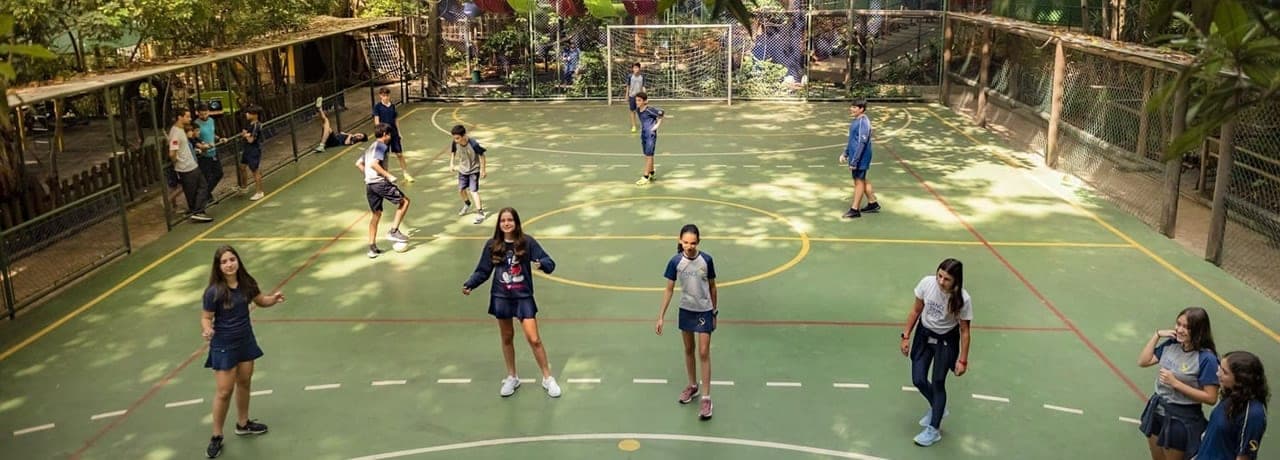 Alunos jogando futebol em quadra poliesportiva ao ar livre