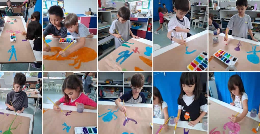 Alunos do 2º ano pintando com aquarela figuras humanas coloridas sobre papel pardo