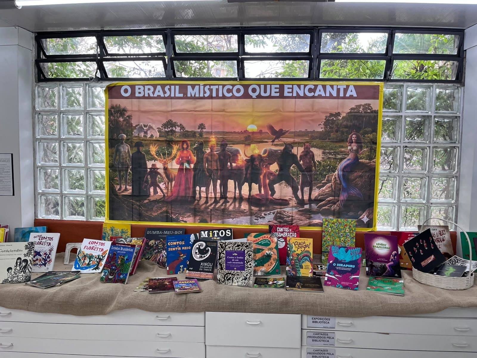 Exposição O Brasil místico que encanta na biblioteca: painel com personagens do folclore e, abaixo, livros sobre o tema
