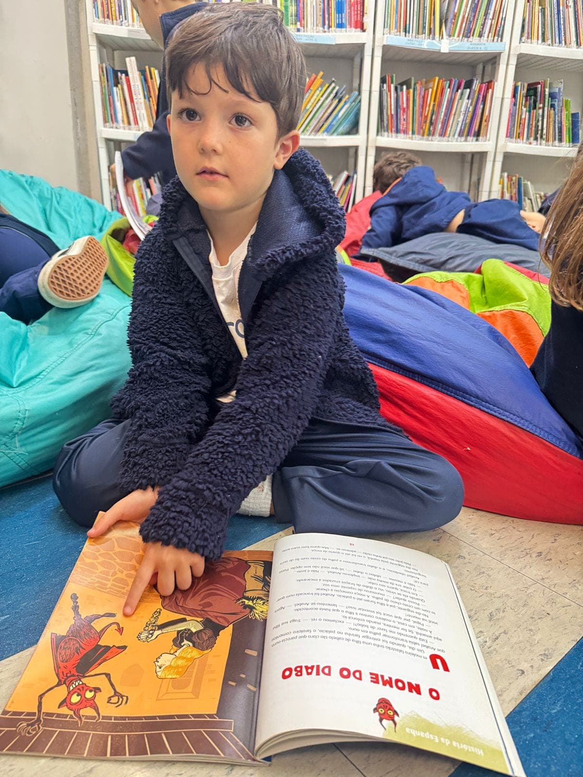 Menino sentado no tapete com um livro ilustrado aberto