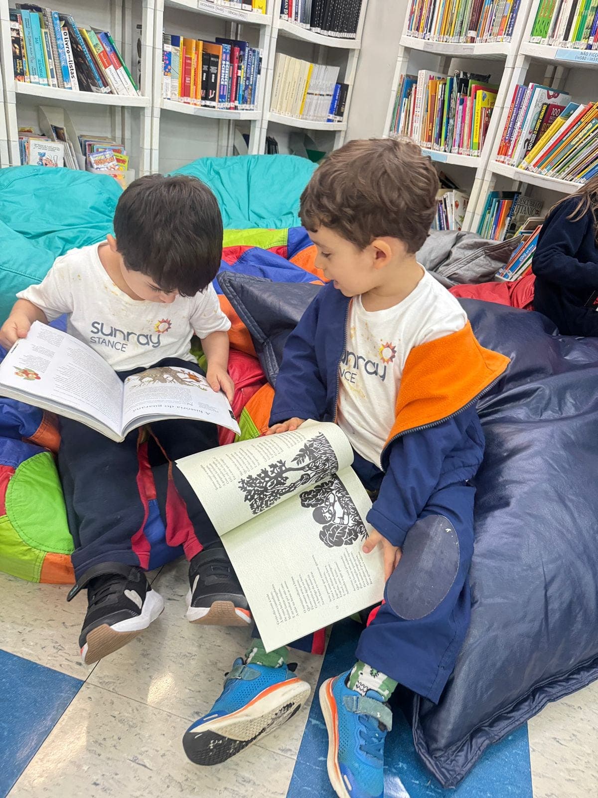 Dois meninos sentados em pufes leem livros da exposição