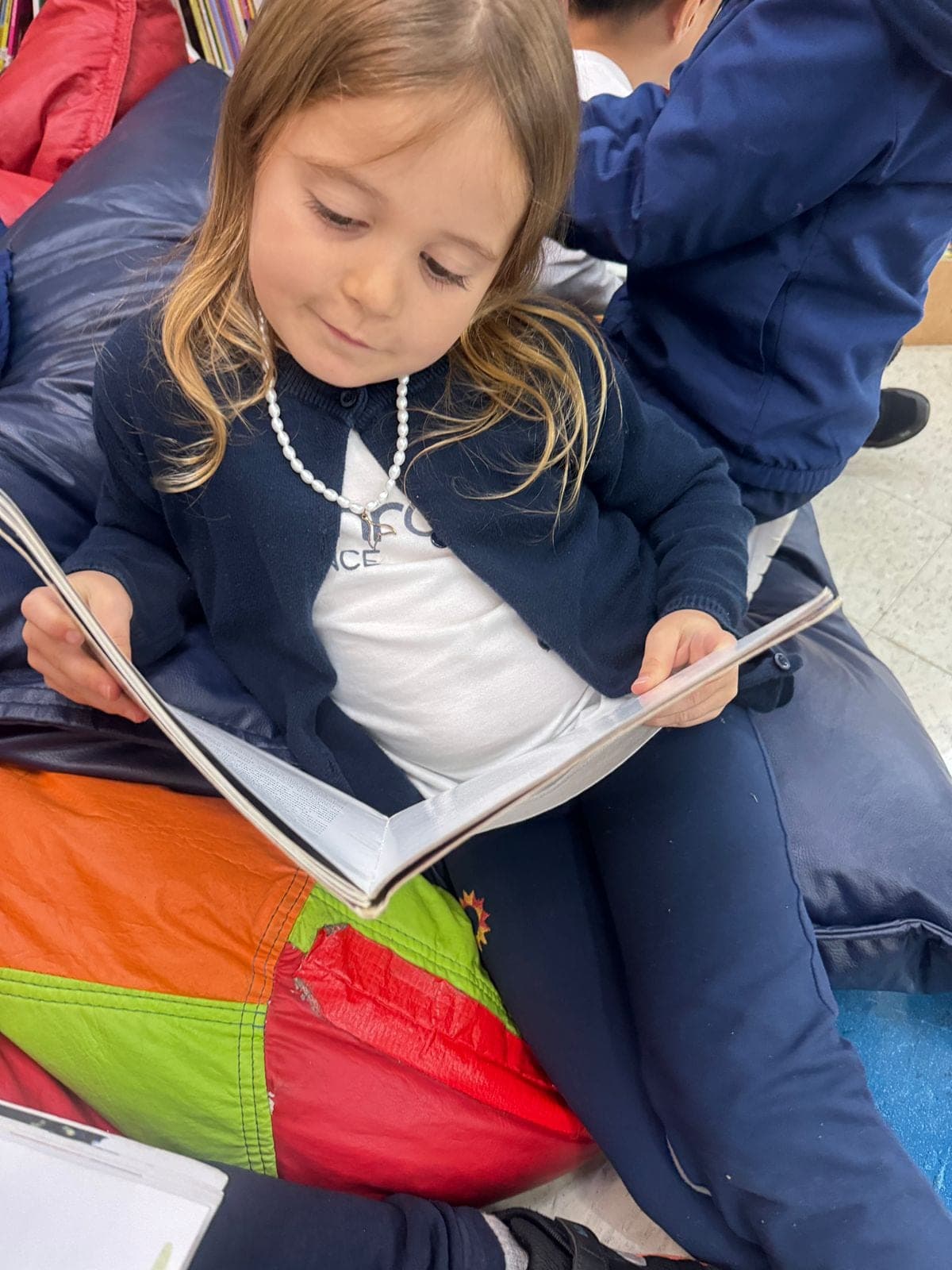 Menina sorridente sentada em um pufe com um livro aberto