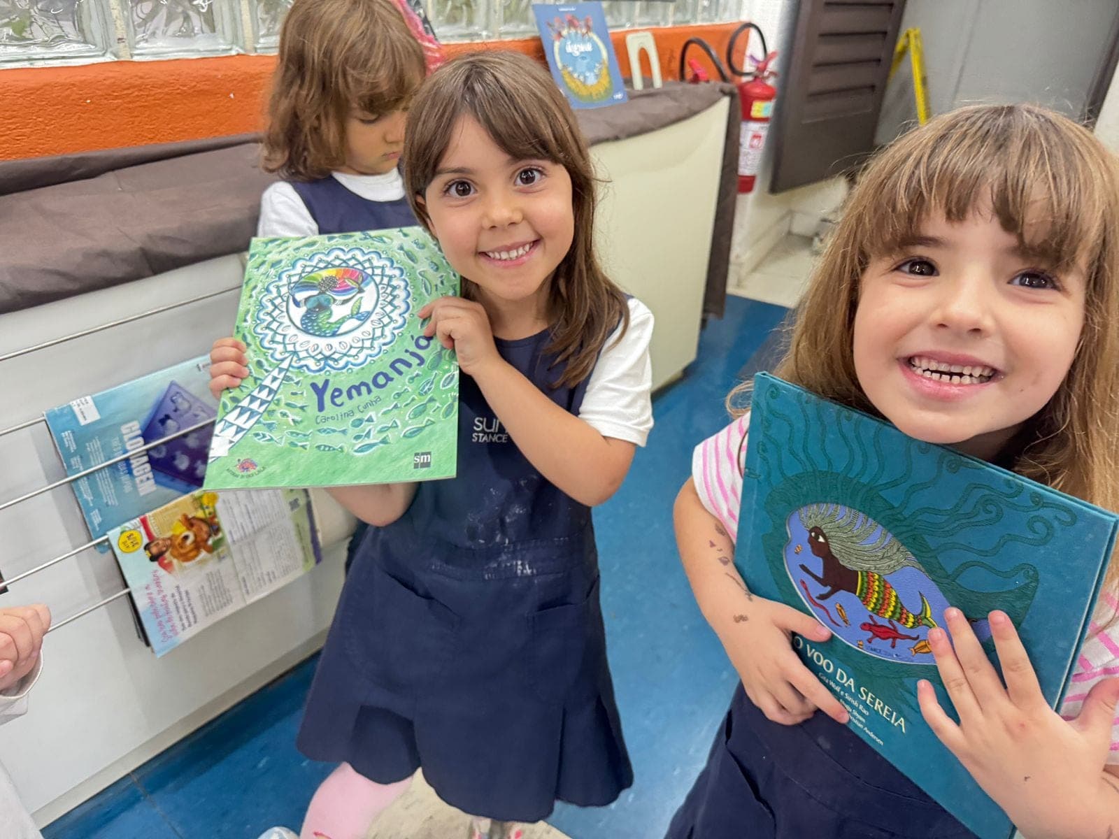 Duas meninas sorriem segurando livros sobre o folclore