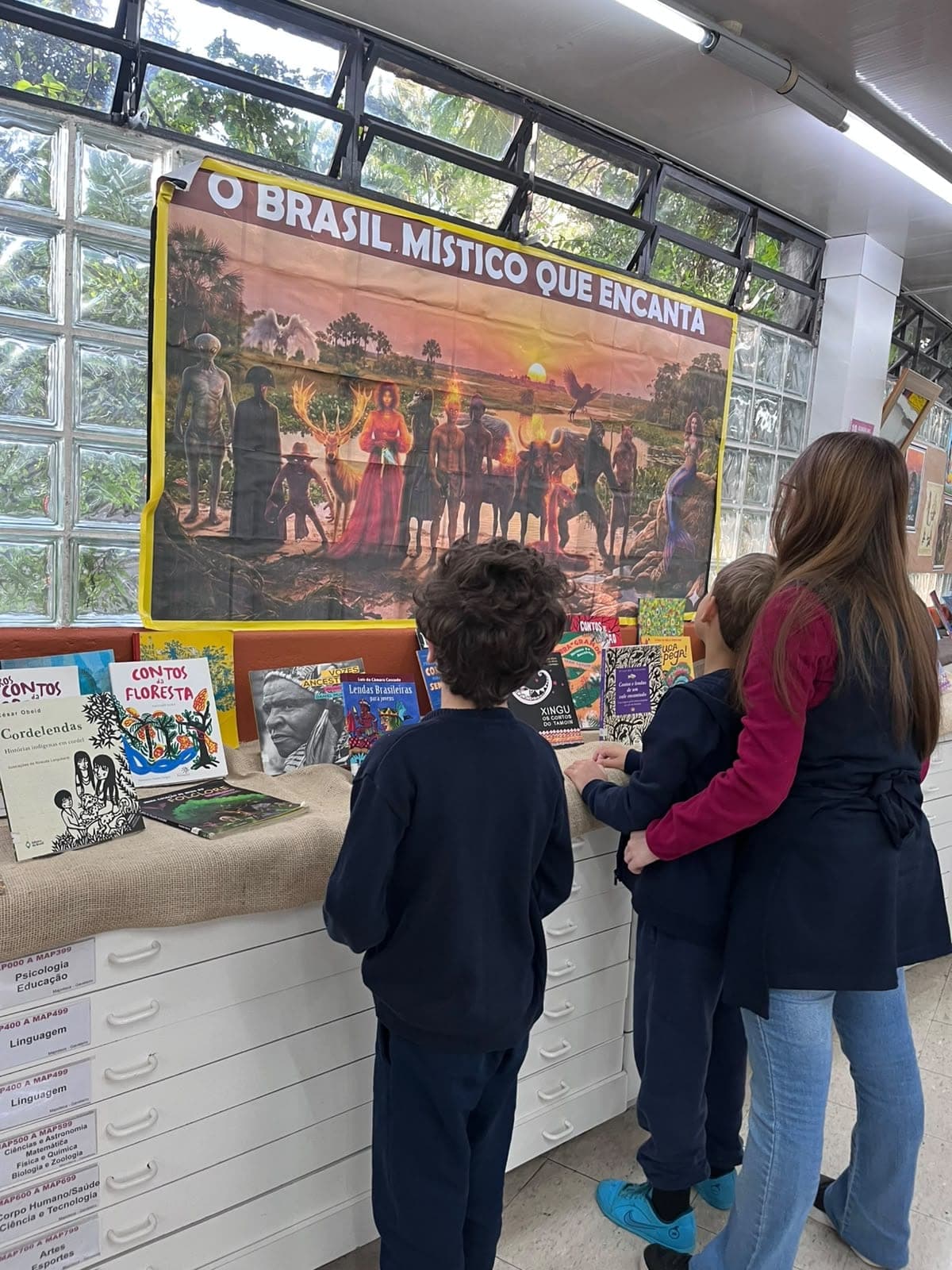 Alunos observam os livros da exposição O Brasil místico que encanta, ao lado de uma professora