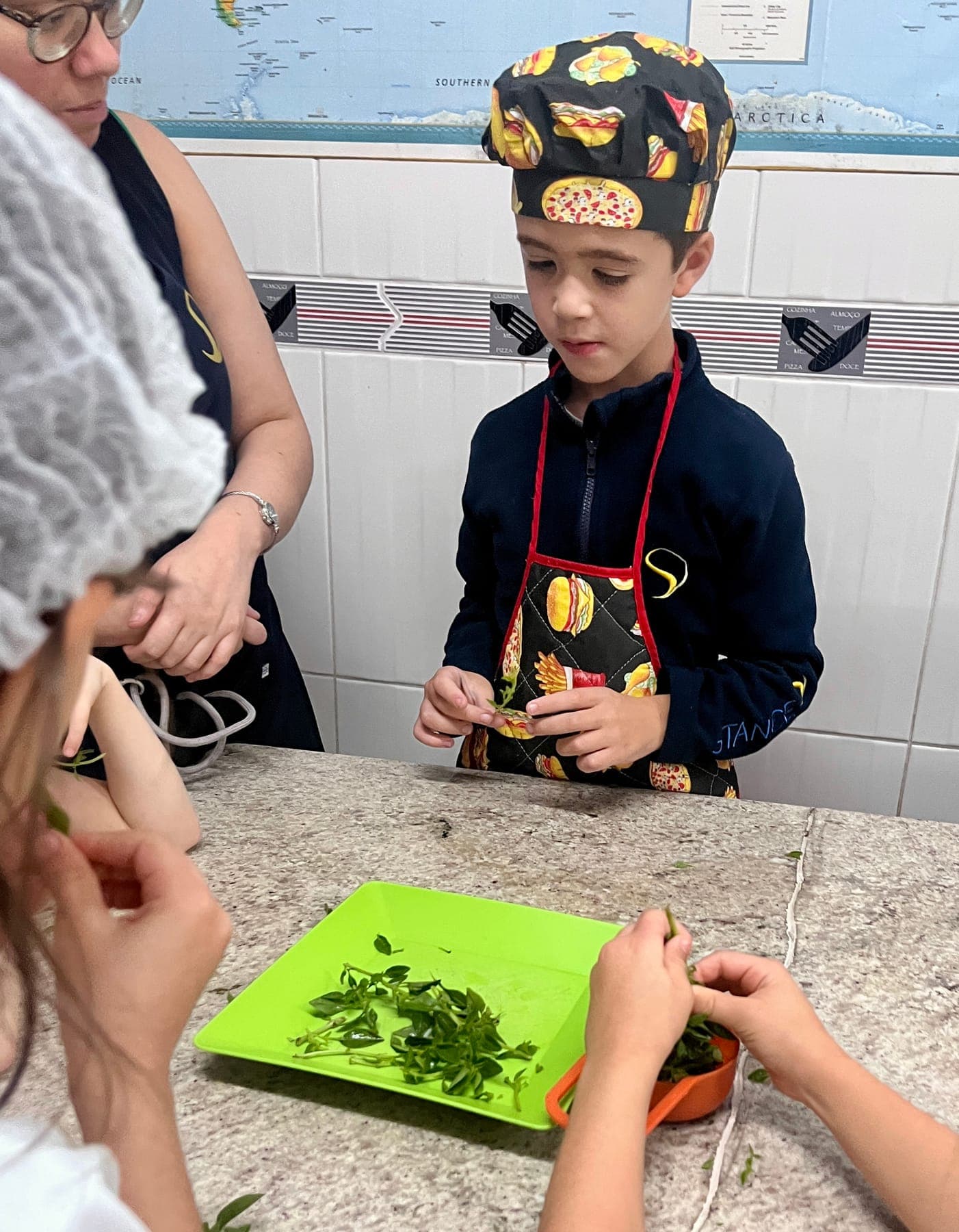 Menino de chapéu de cozinheiro diante de uma bandeja verde com folhas de manjericão