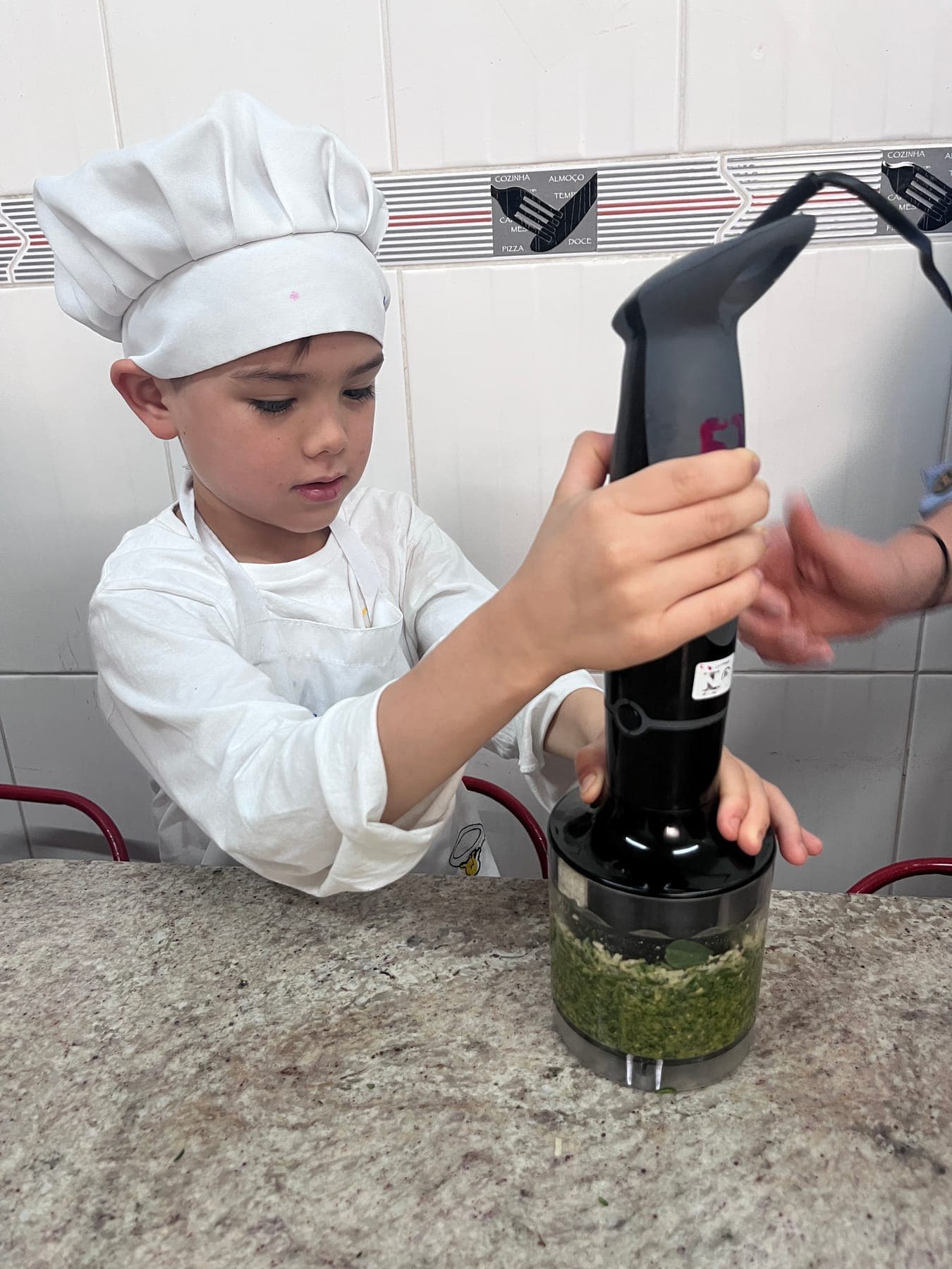Menino de chapéu de cozinheiro bate o pesto com o mixer