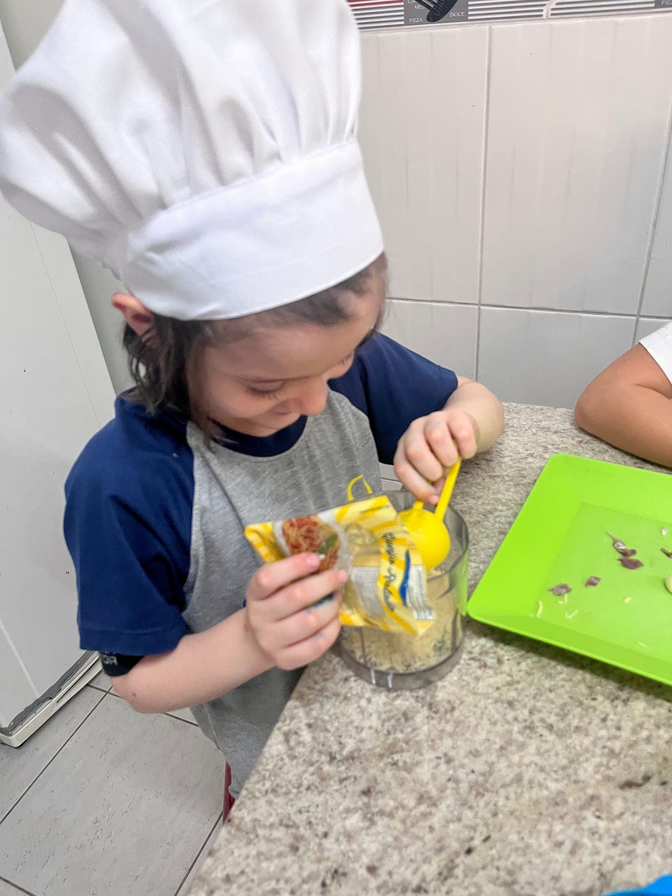 Menina de chapéu de cozinheiro acrescenta queijo parmesão ralado ao pote