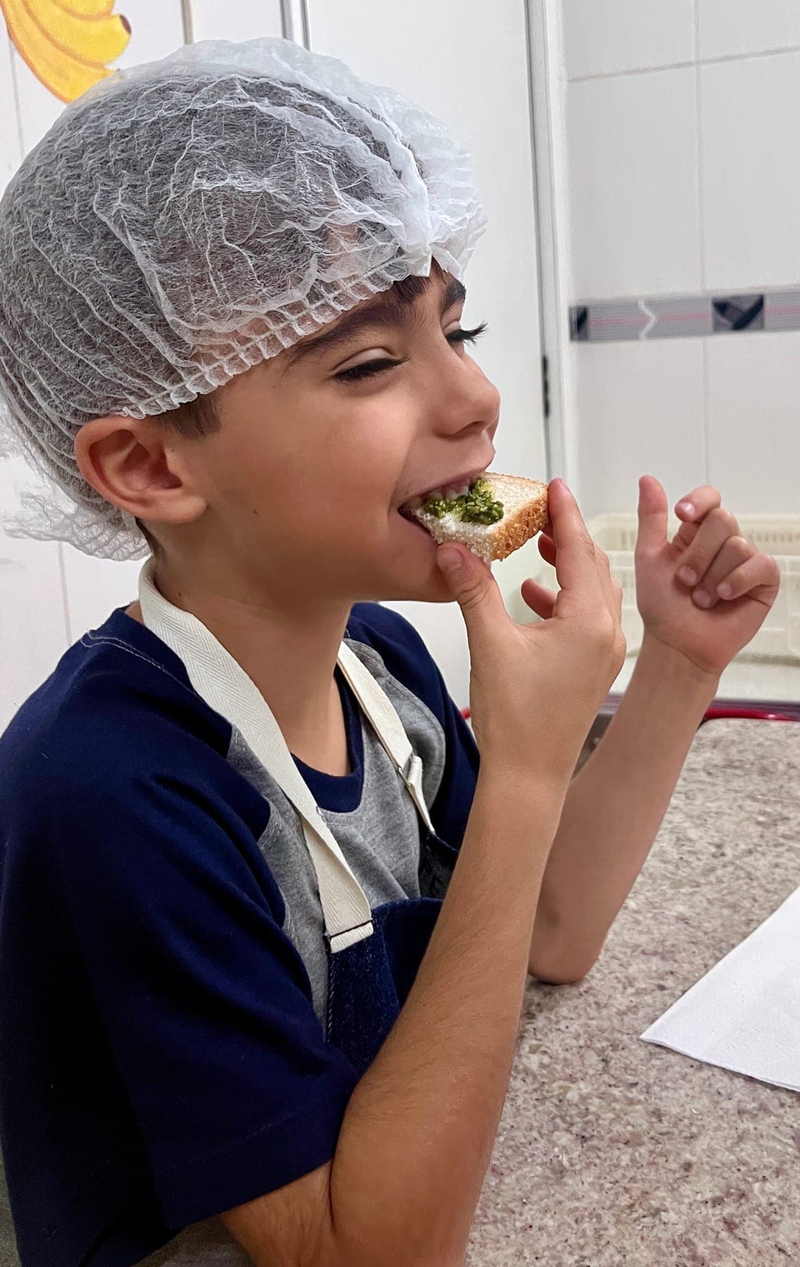 Menino de touca prova uma torrada com pesto