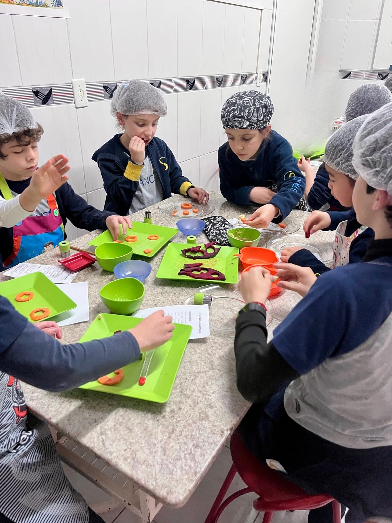 Turma do Y2 e do Y3 reunida à mesa preparando os legumes para comer com o homus