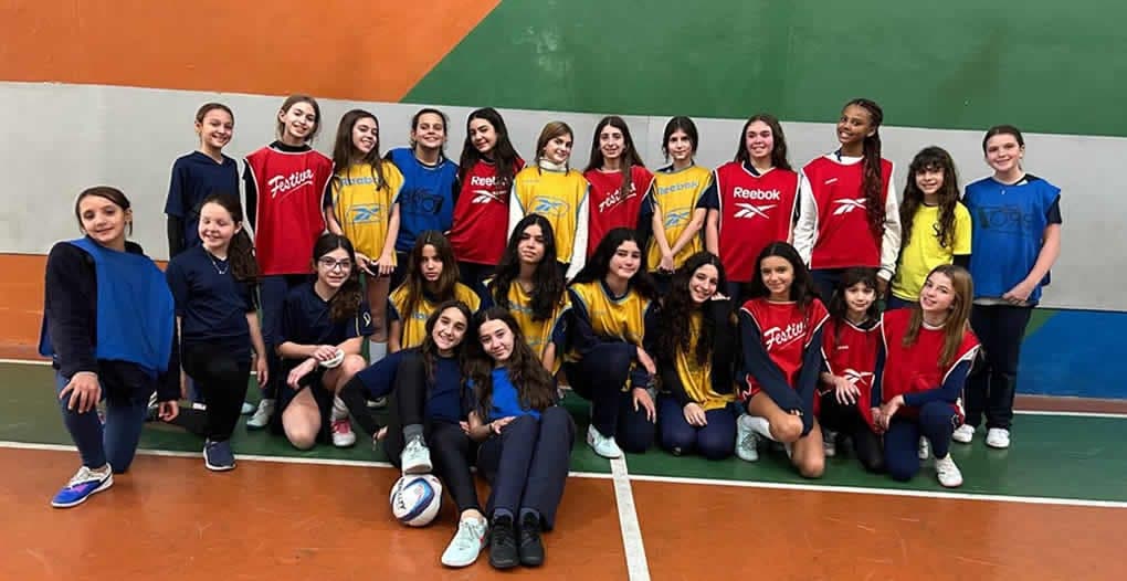Alunas do futsal feminino reunidas na quadra com coletes azuis, vermelhos e amarelos