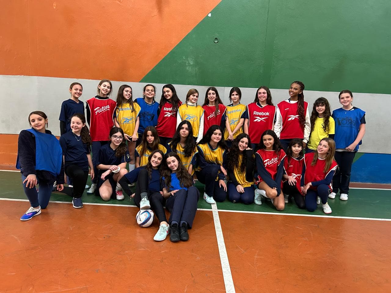 As três equipes de alunas reunidas com coletes azuis, vermelhos e amarelos na quadra após o torneio de futsal