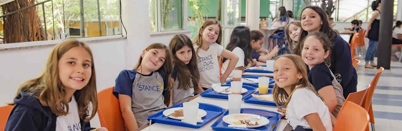 Alunas sorridentes almoçando juntas com bandejas no restaurante da escola