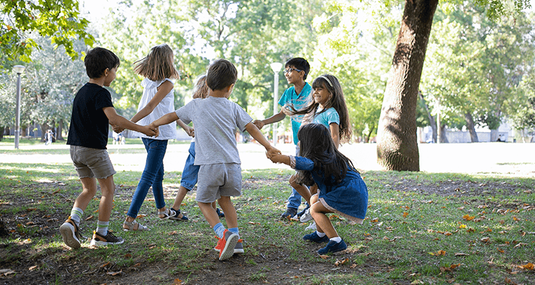 Crianças de mãos dadas brincando de roda na grama de um parque