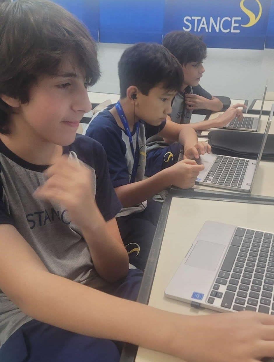 Alunos de uniforme da Stance trabalham em notebooks, lado a lado, em sala de aula