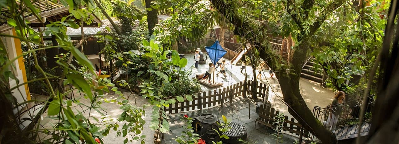 Crianças brincando em pátio arborizado da Educação Infantil, com cercas de madeira e muitas plantas