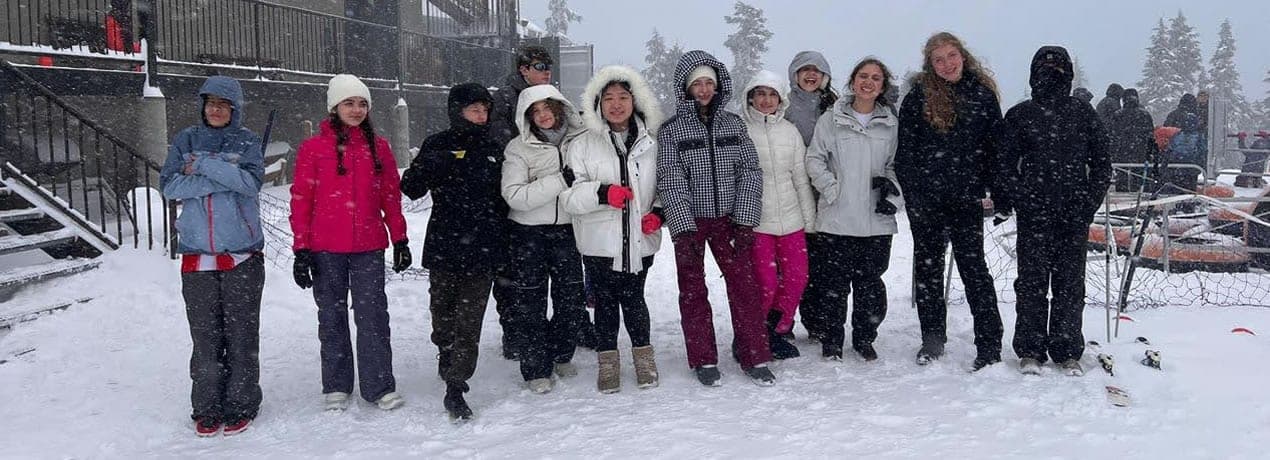 Grupo de alunos com roupas de inverno posando na neve durante o Programa Internacional Canadá