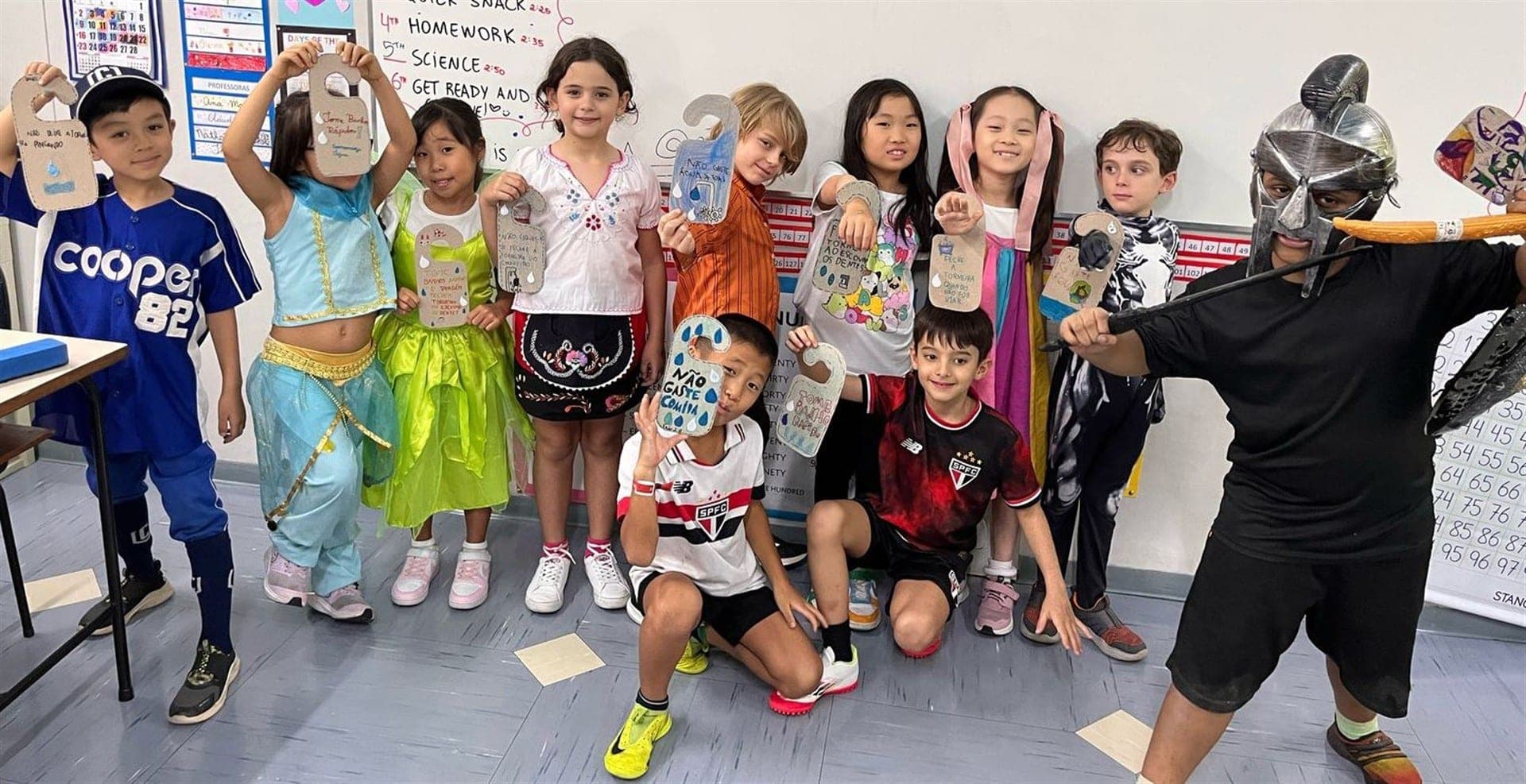 Alunos do 2º ano B fantasiados mostram os marcadores de porta com dicas como Não gaste comida e Tome banho rápido
