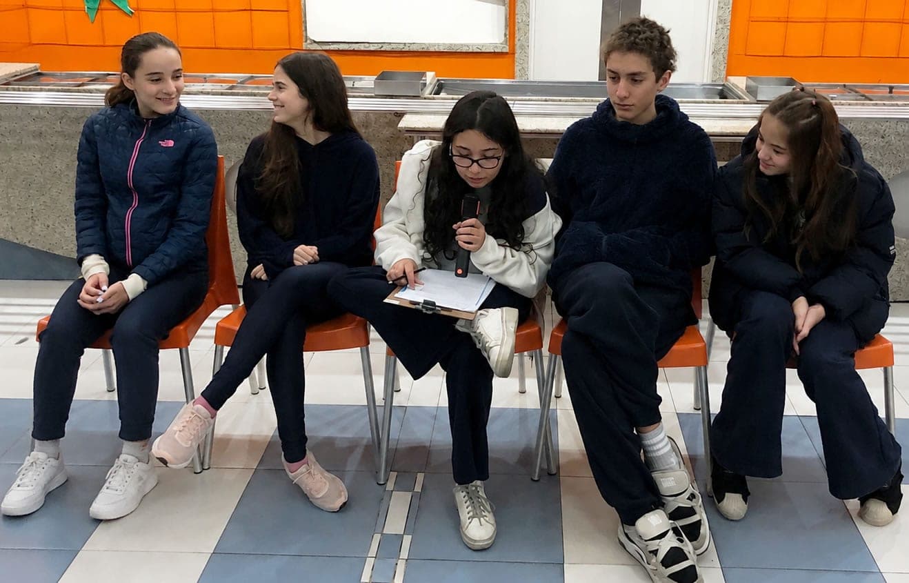 Alunos do 8º ano sentados lado a lado na simulação de julgamento; uma aluna lê ao microfone