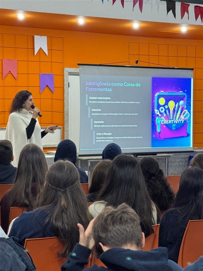 Juliana Caetano fala ao microfone para alunos do 9º ano diante do slide "Inteligência como Caixa de Ferramentas"