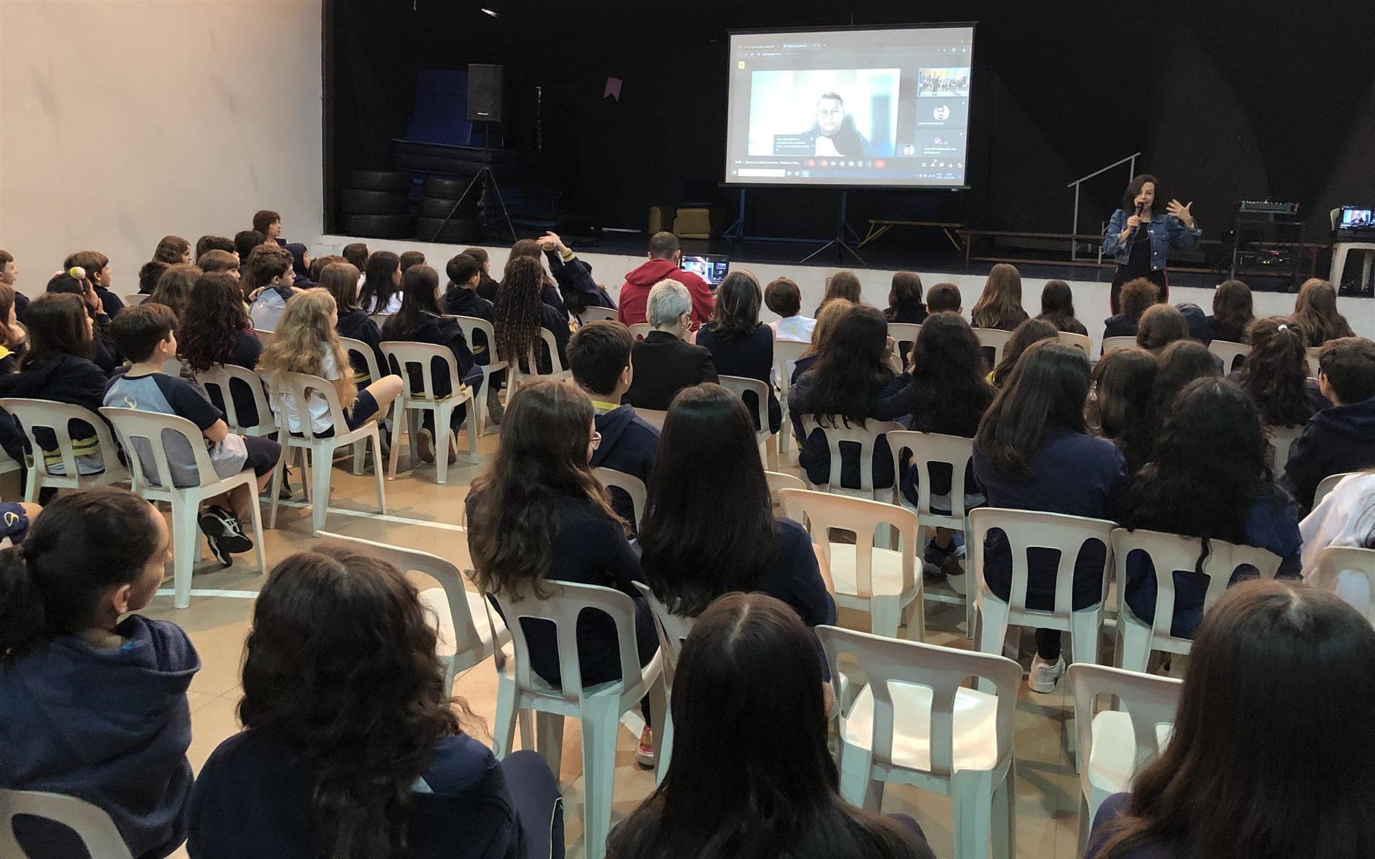 Alunos no auditório acompanham Maickson Serrão por videochamada projetada no telão