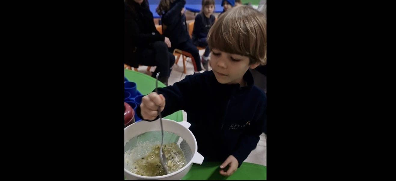 Criança do Kinder mexe com uma colher a mistura em uma peneira durante a oficina de reaproveitamento de alimentos