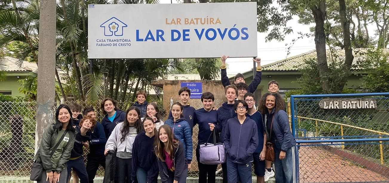 Alunos e educadoras em frente à placa do Lar Batuíra, Lar de Vovós