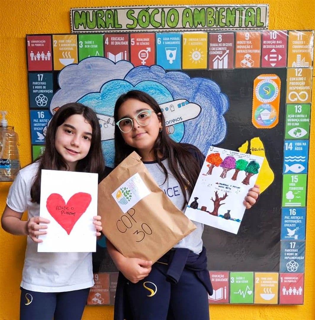 Alunas do 5º ano mostram desenhos e envelope da COP30 em frente ao Mural Socioambiental