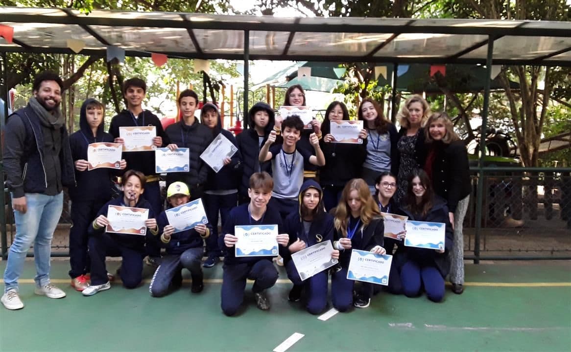 Grupo de alunos premiados no Canguru segura certificados ao lado de professores no pátio da escola