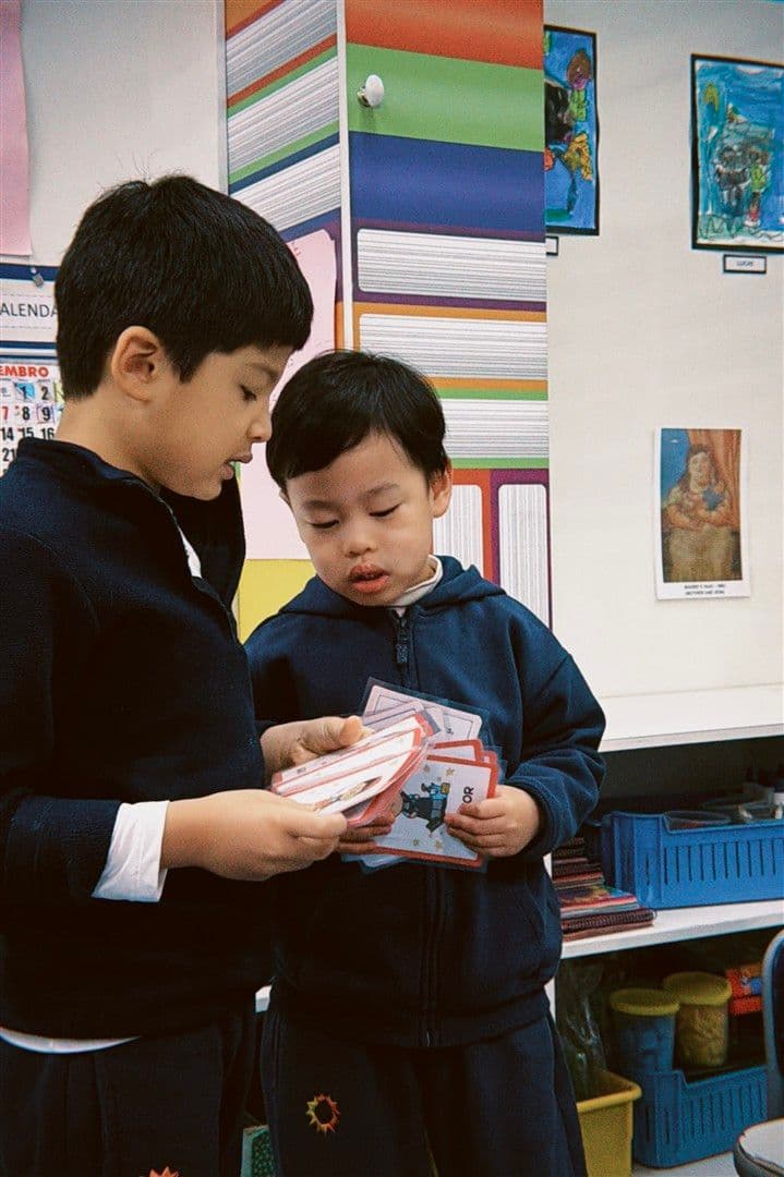 Dois meninos de uniforme dividindo um maço de cartas ilustradas na sala de aula