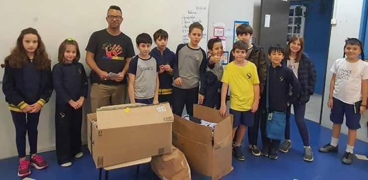 Alunos do 5º C com caixas de agasalhos ao lado do representante do Projeto Mão Amiga