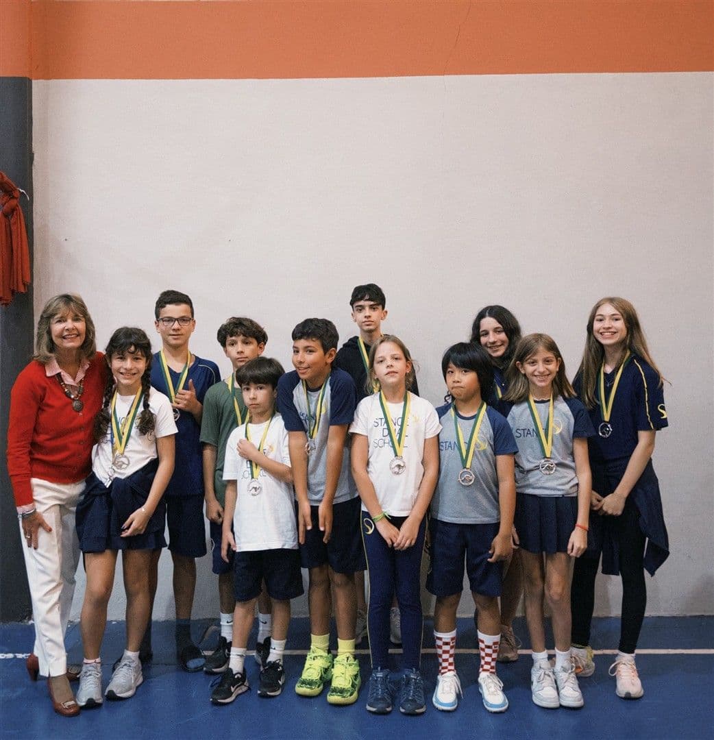 Alunos com medalhas de prata do Canguru de Matemática posam ao lado de uma educadora na quadra