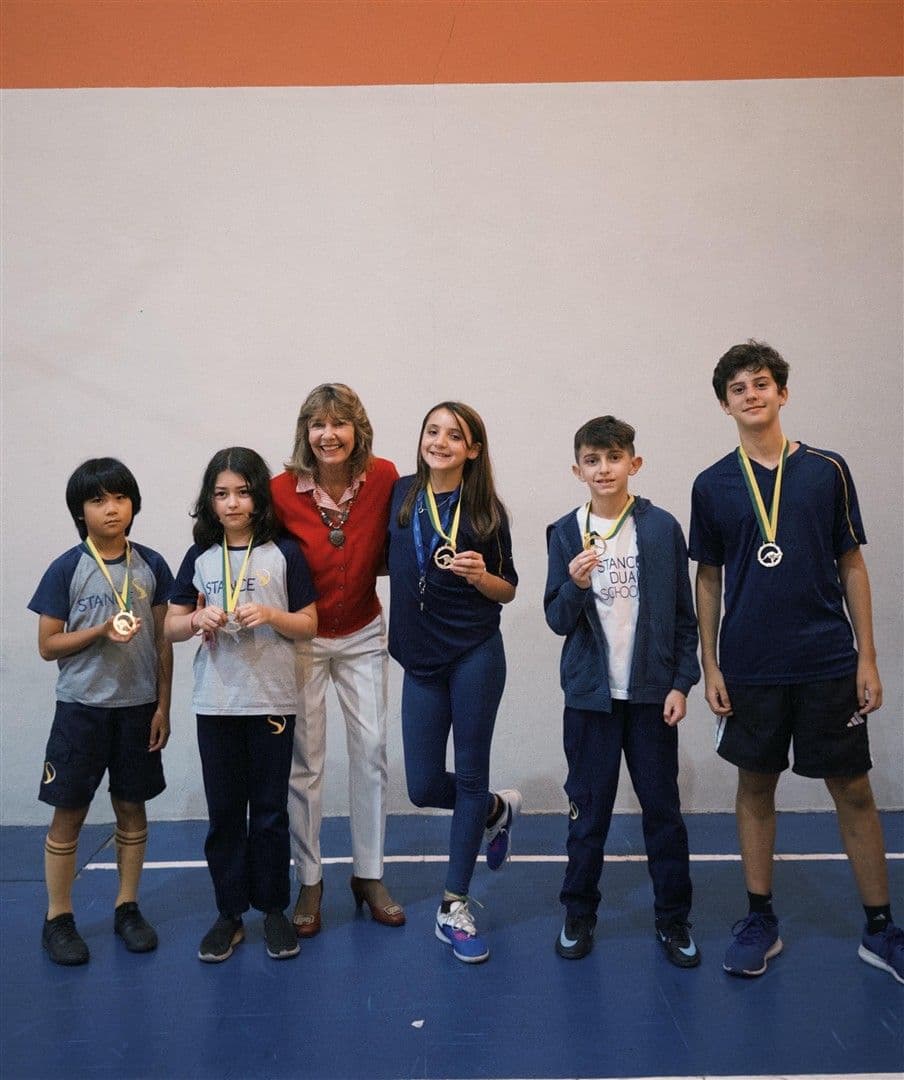 Cinco alunos com medalhas de ouro do Canguru de Matemática posam ao lado de uma educadora na quadra