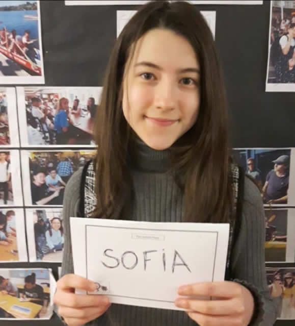 Ex-aluna Sofia sorrindo e segurando uma folha com o nome "Sofia"