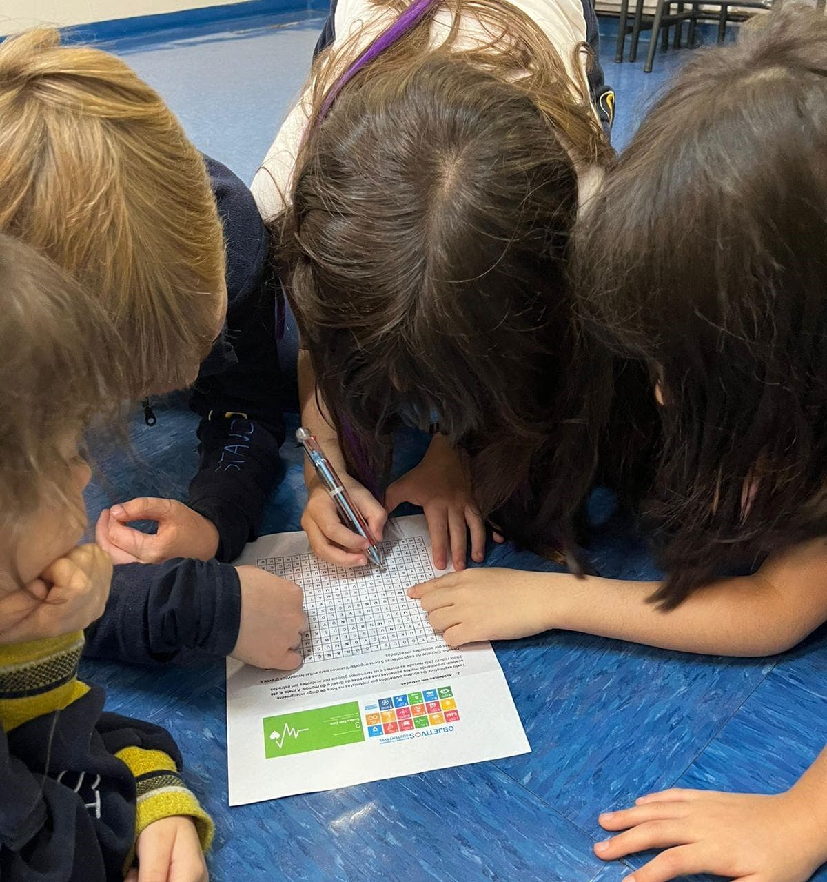 Alunas debruçadas no chão resolvem caça-palavras sobre os Objetivos de Desenvolvimento Sustentável na Gincana Sustentável