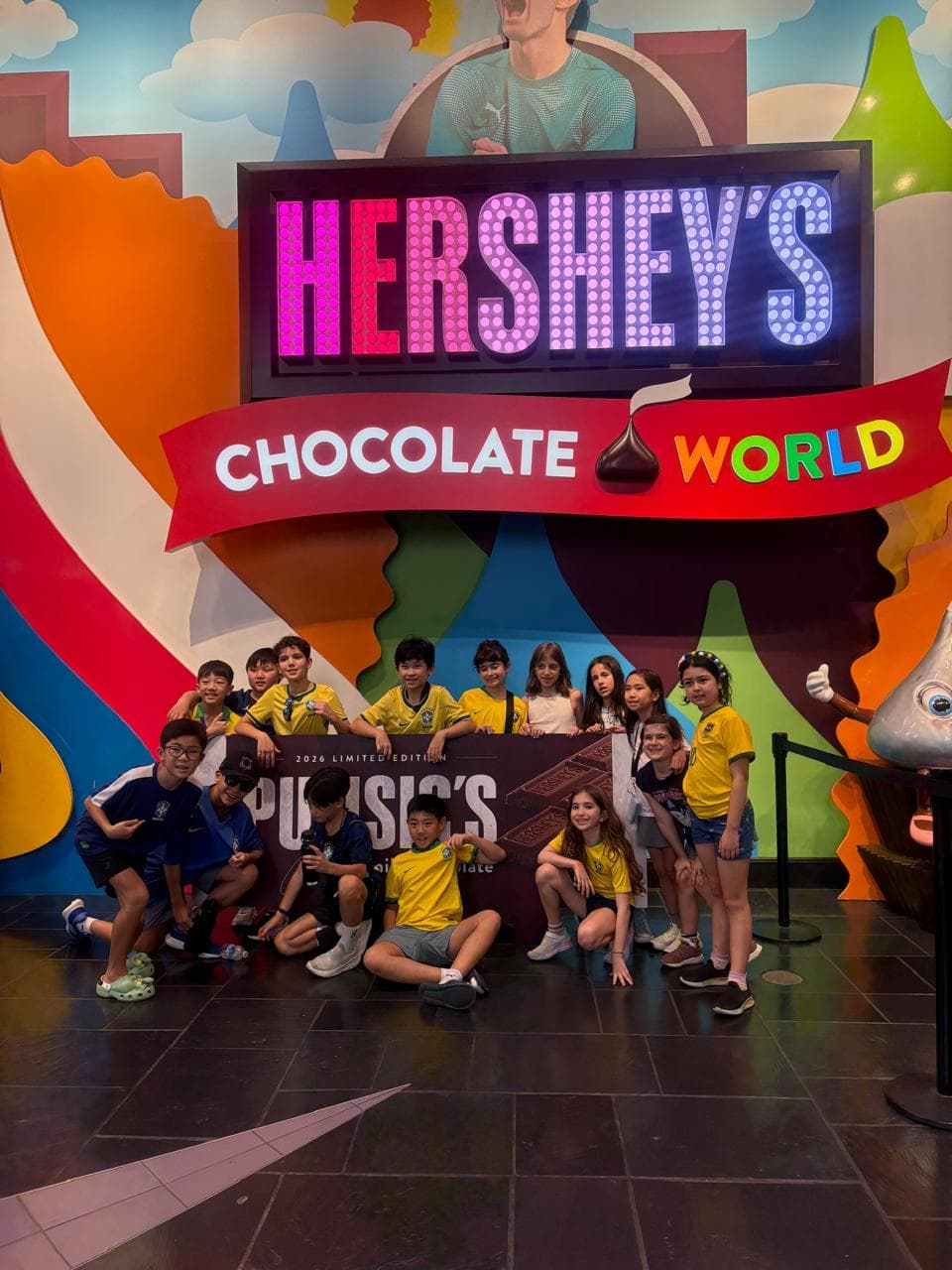 Grupo de alunos, vários com a camisa do Brasil, posa sob o letreiro Hershey's Chocolate World