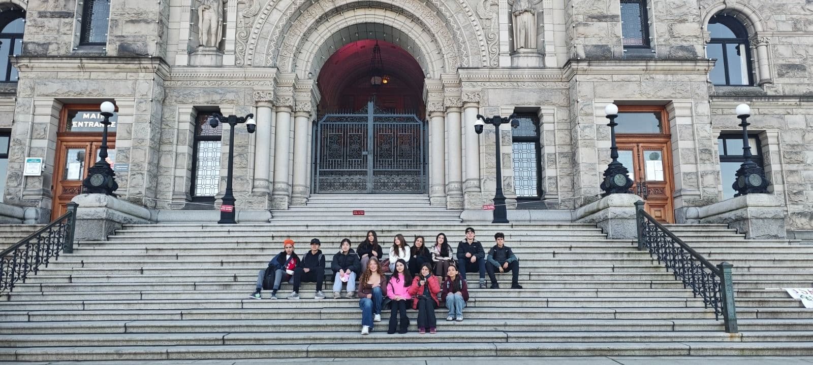 Alunos sentados na escadaria de um edifício histórico de pedra em Victoria