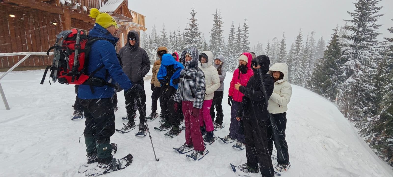 Alunos com raquetes de neve ouvem as orientações de um guia sob a neve