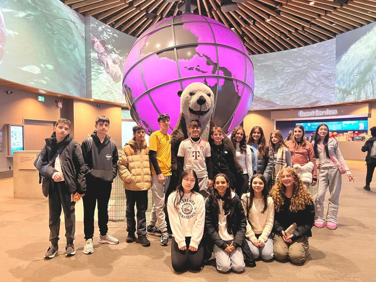 Alunos em grupo diante de um globo iluminado e de um mascote de urso polar