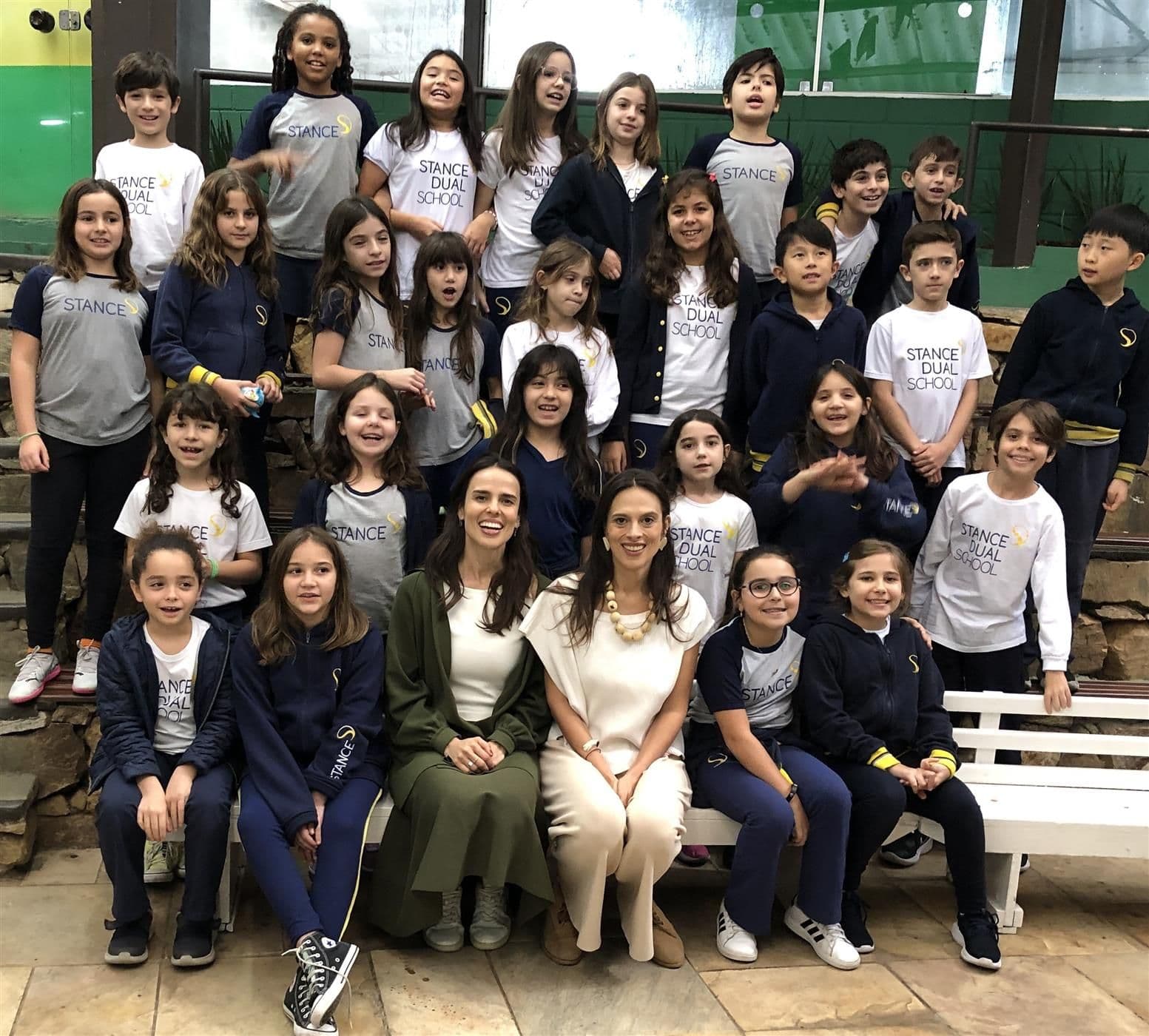 Turma do 4º ano reunida em foto com as duas convidadas sentadas no banco à frente