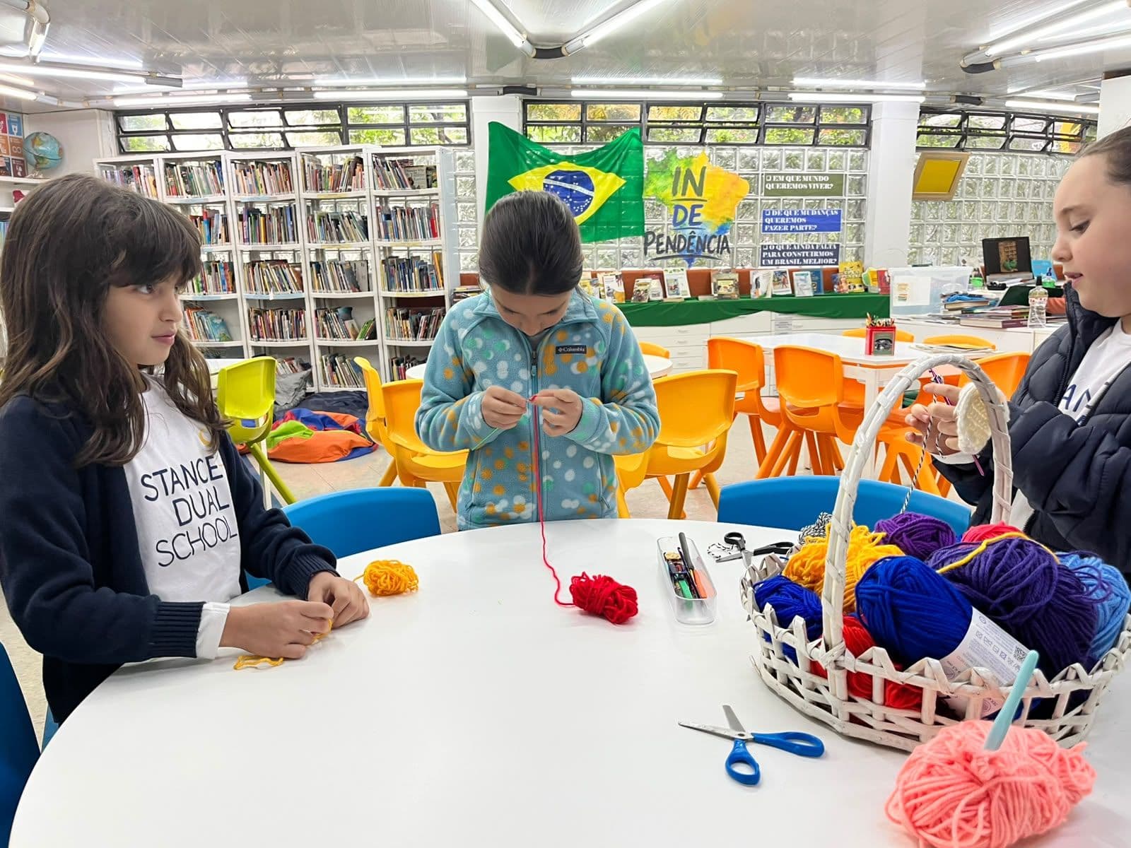 Alunas fazem trabalhos com fios de lã coloridos em mesa da biblioteca durante o recreio