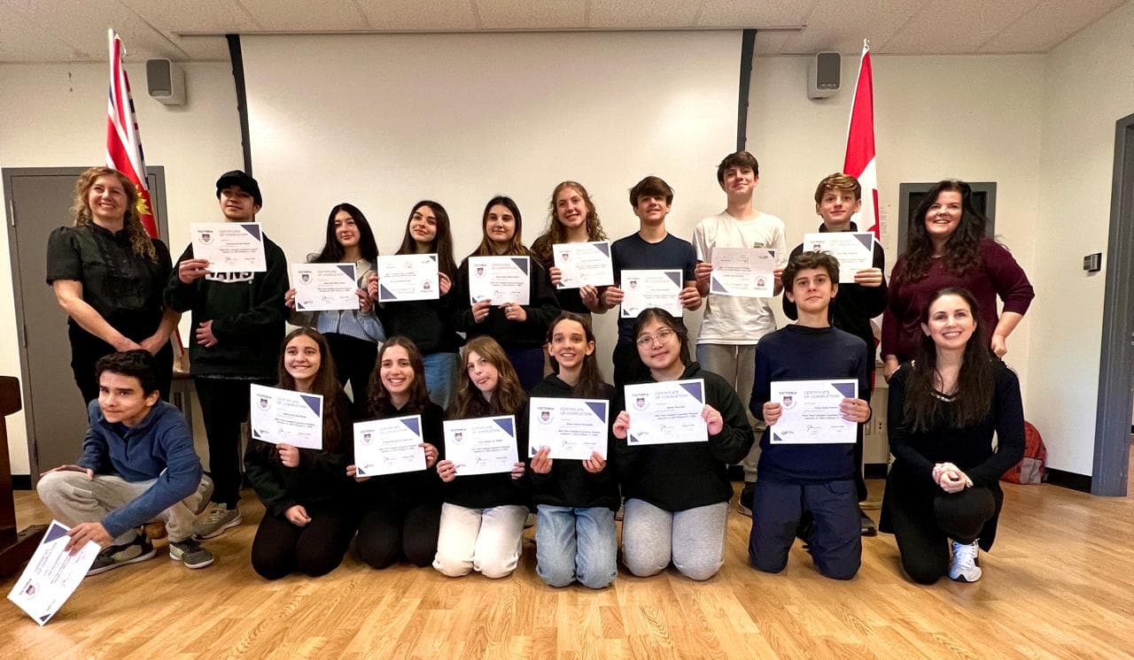 Alunos exibem certificados de conclusão ao lado das professoras, entre bandeiras do Canadá
