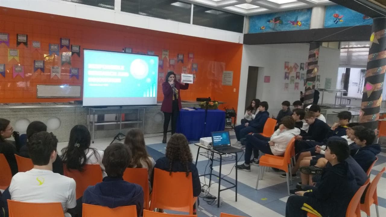 Palestrante fala a alunos sentados diante de telão com slide sobre pesquisa e inovação responsável