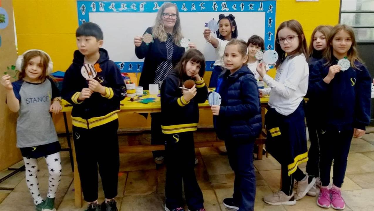 Alunos e professora mostram tartarugas de papel feitas na oficina de produção artesanal