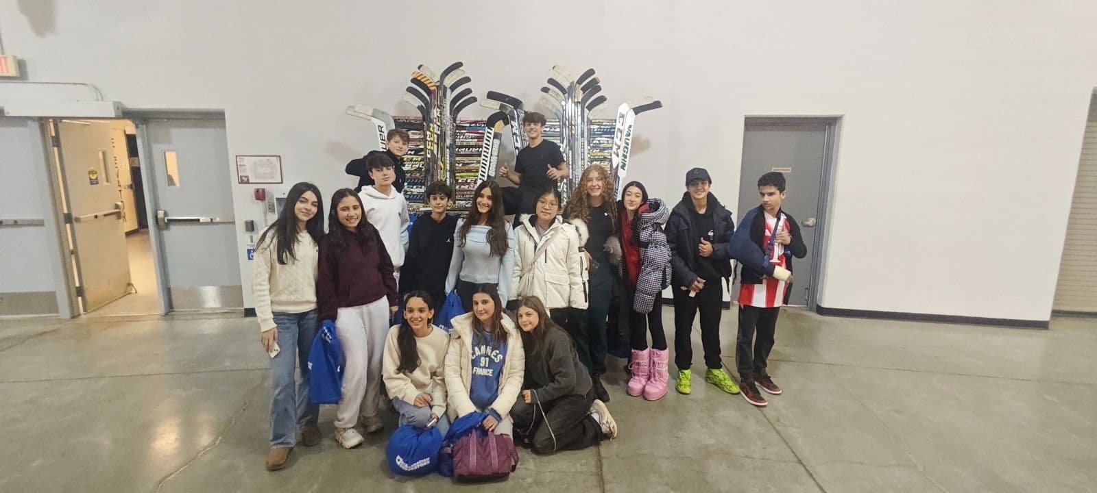 Alunos posam diante de uma parede de tacos de hóquei em um ginásio