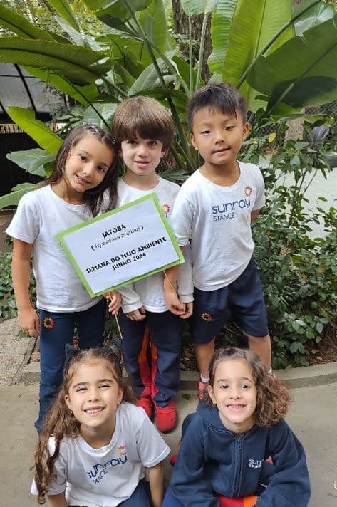 Crianças da Educação Infantil posam no jardim com placa: Jatobá, Semana do Meio Ambiente, junho 2024