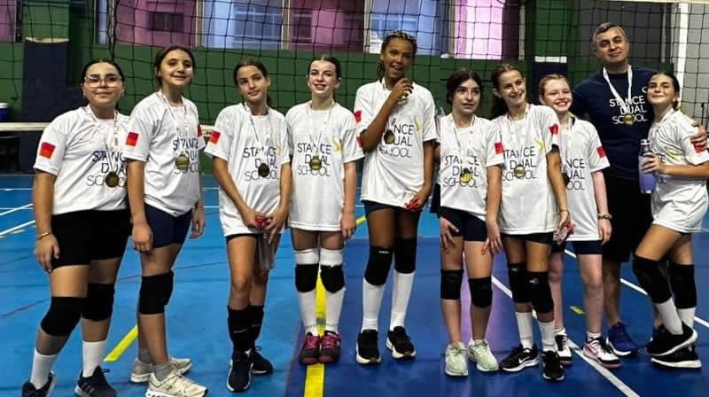 Equipe feminina de vôlei da Stance posa com medalhas na quadra ao lado do técnico