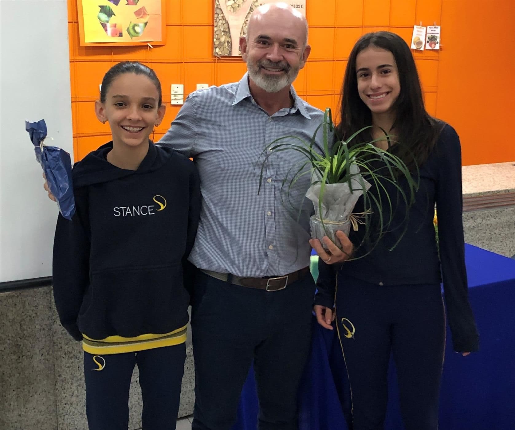 Domingo Melero Sancho posa entre duas alunas, segurando um vaso de planta recebido de presente