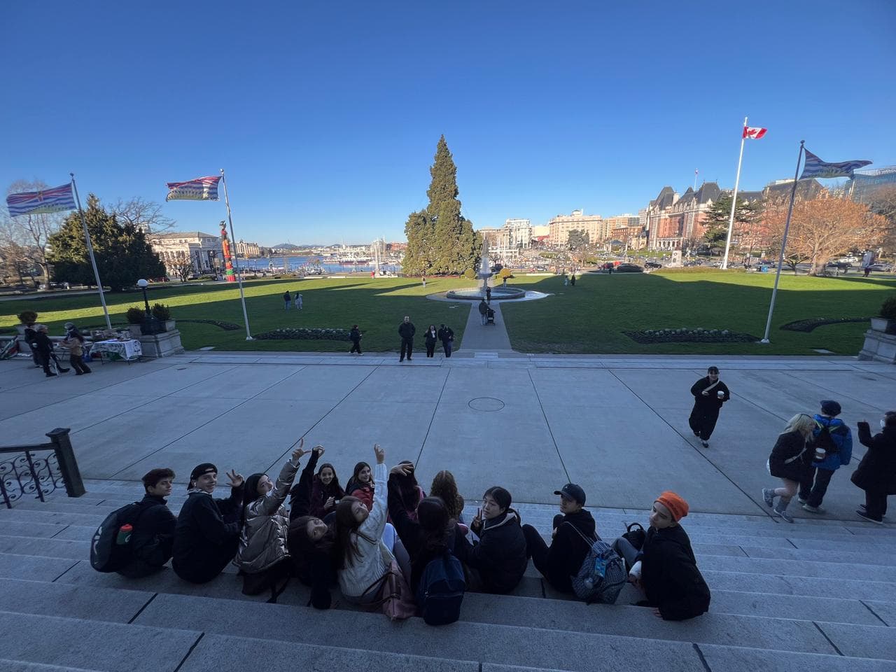 Alunos sentados em escadaria diante de um gramado com fonte, bandeiras do Canadá e da Colúmbia Britânica e prédios ao fundo